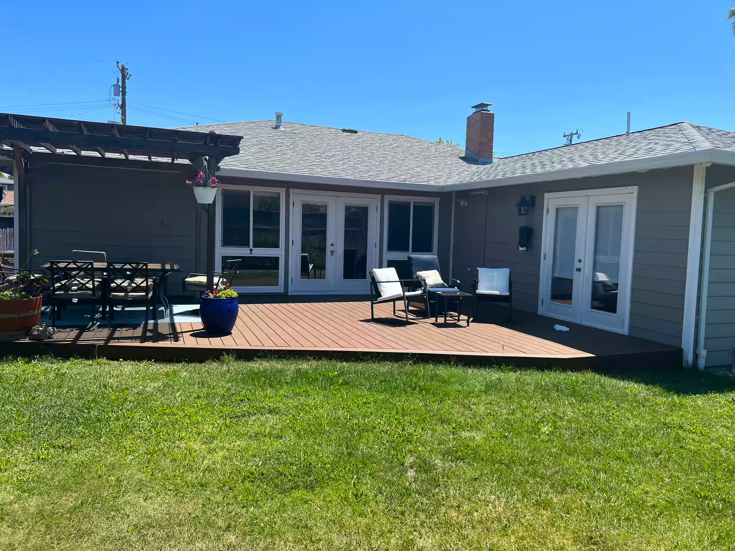 Backyard deck with a dining table, lounge seating, and a pergola, overlooking the lawn