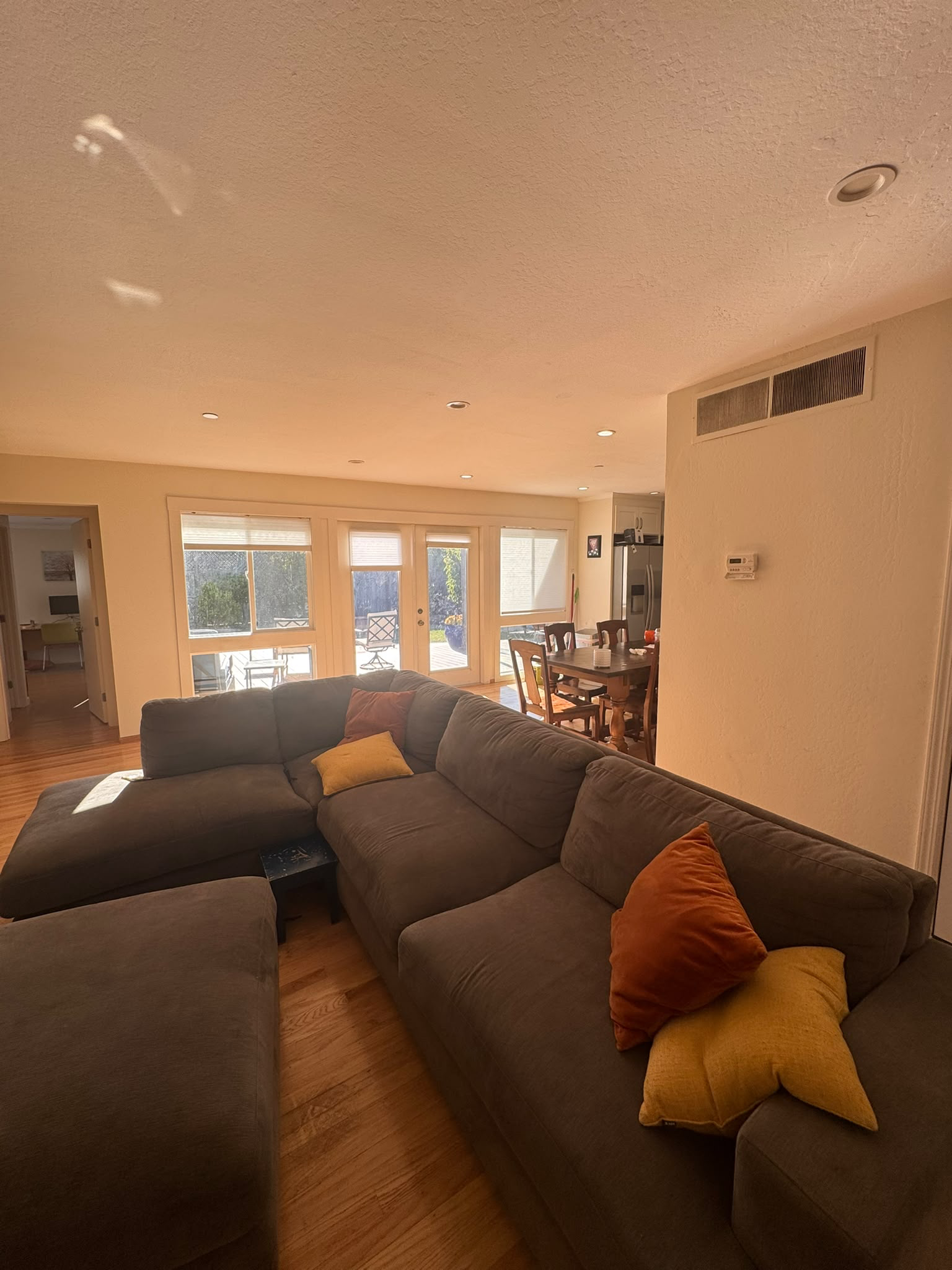 Living room with a large sectional sofa, hardwood floors, and views to the backyard and dining area